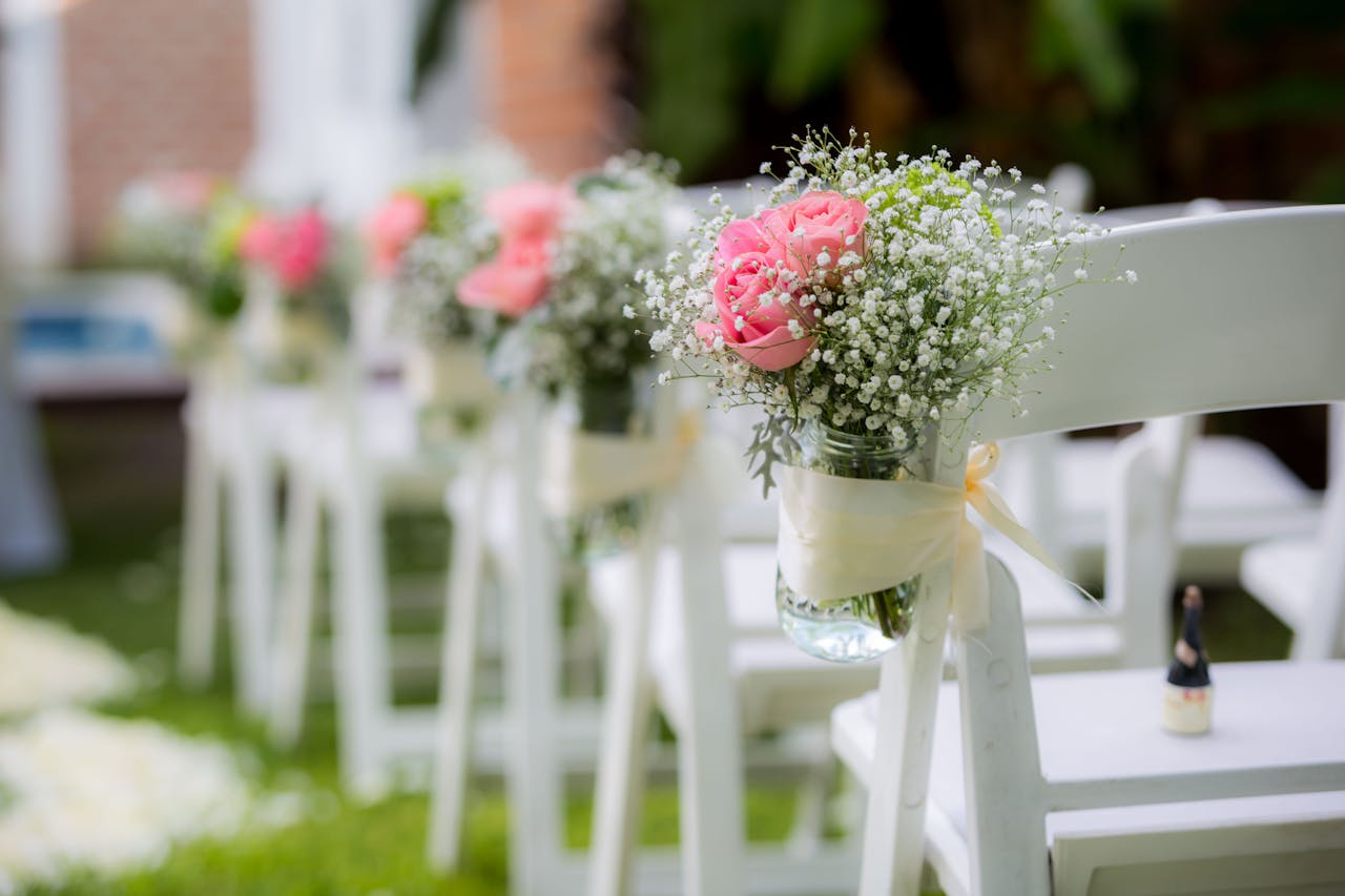 White folding chairs adorned with pink roses and baby's breath, ideal for weddings.